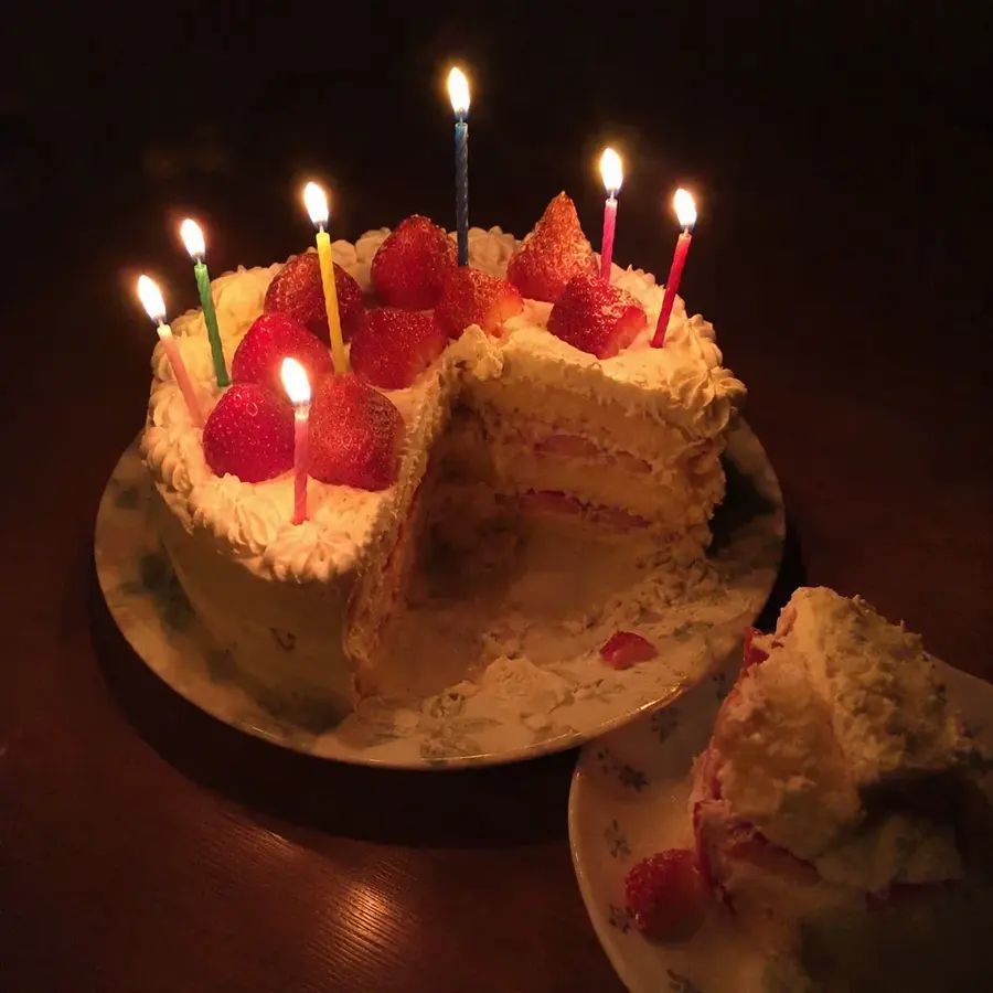 ろうそくが灯った、ひと切れ取り分けられた苺の誕生日ケーキ